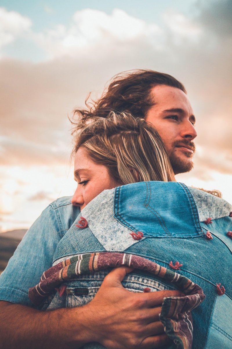 sitting woman leaning on man's shoulder facing lake during golden hour